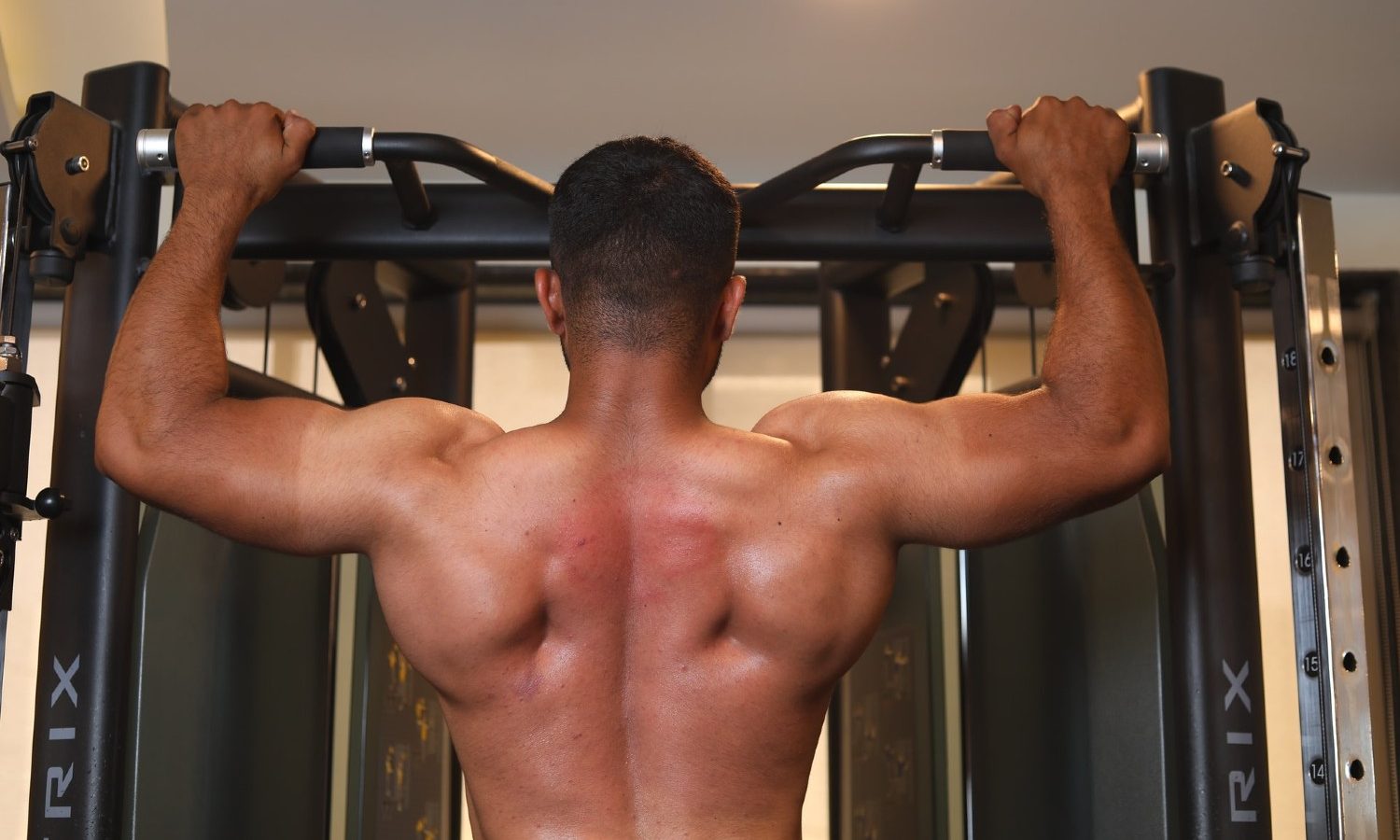 Shirtless man doing a shoulder workout on a pull-up bar.