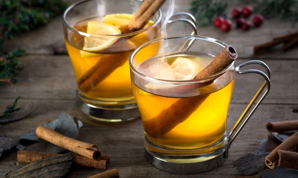 Two glasses of hot toddies with cinnamon sticks on a wooden table.