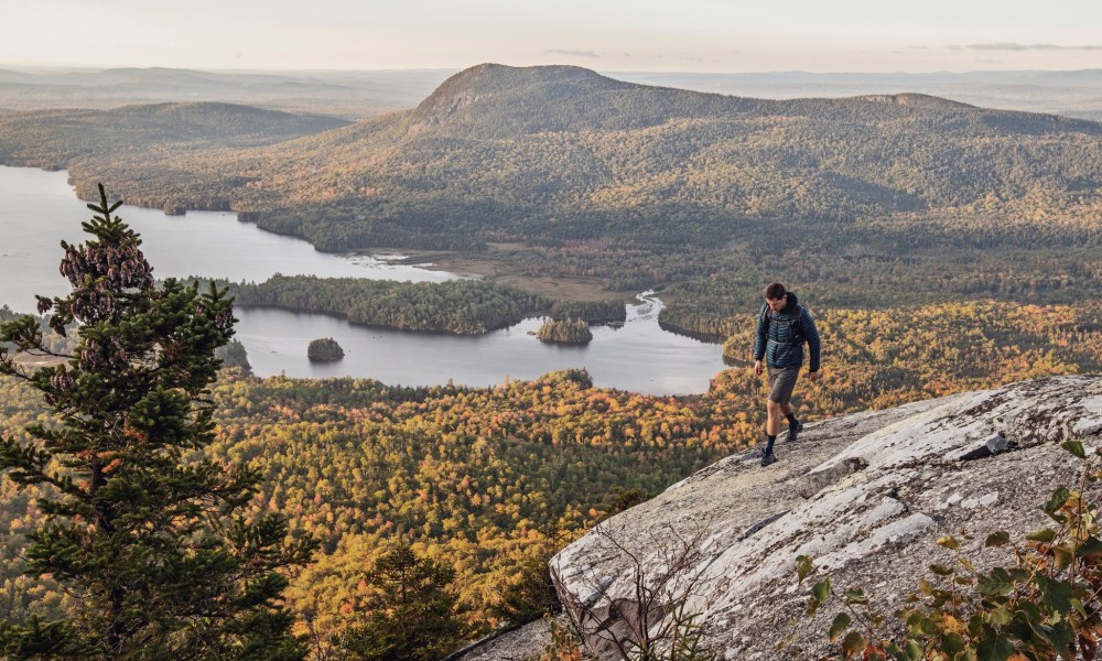 Male hiker walks along cliff with view on Appalachian Trail, Maine.