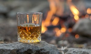 Whiskey in a crystal glass sitting on a rock in front of a fire