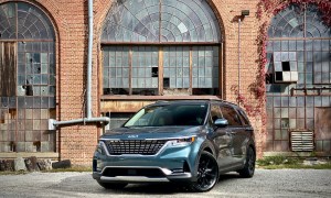 Kia Carnival front end angle from driver side in front of old building.