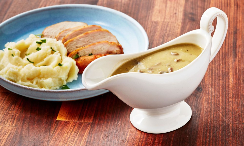 A giblet gravy served in a gravy boat beside a plate of turkey slices