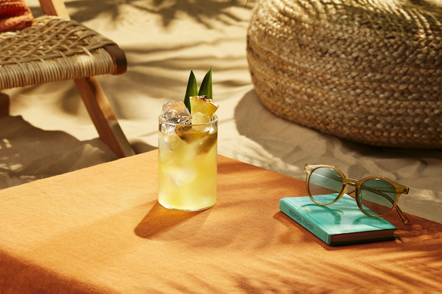 A glass of Life's a Beach cocktail beside a book and sunglasses on a beach table.