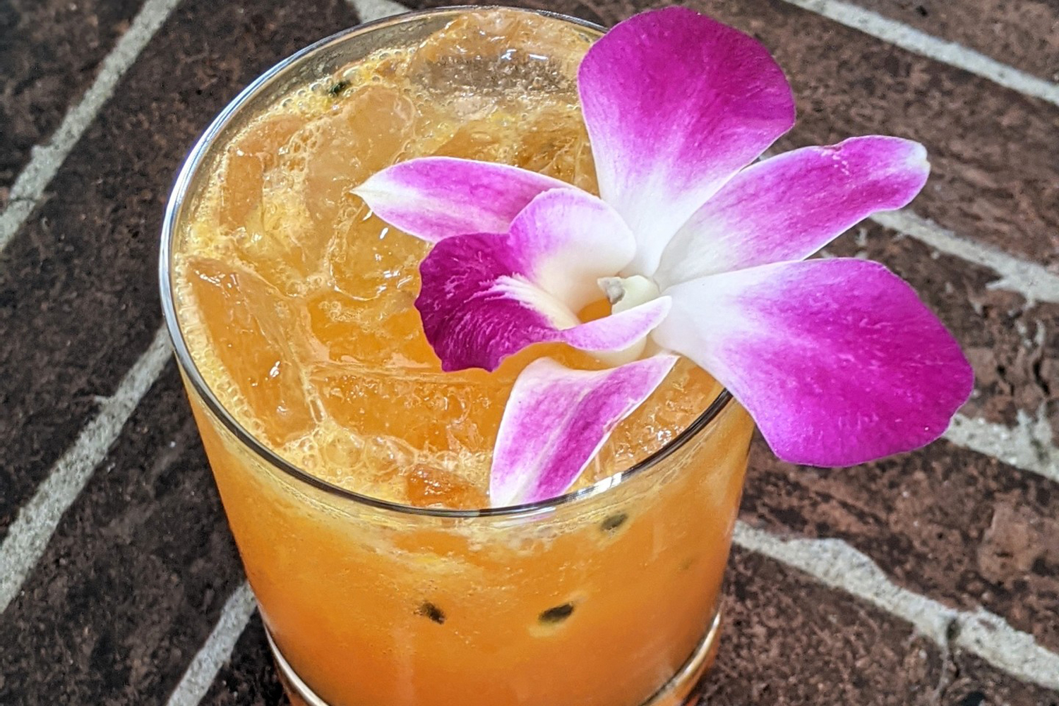 A closeup of a glass of Passion Project cocktail with orchid flower on a table.