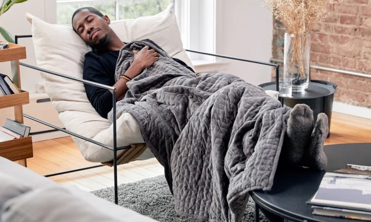 A man sleeping on a chair with a weighted blanket in a room.