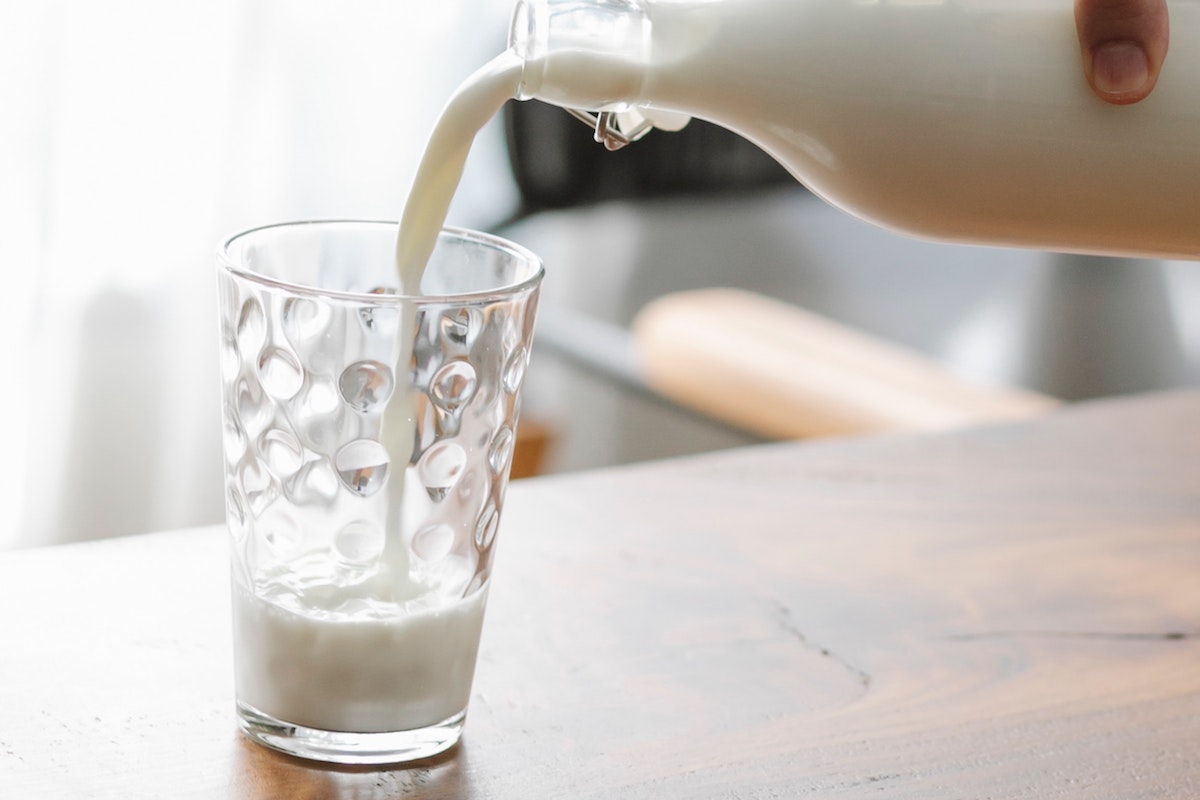 Person pouring a glass of milk.