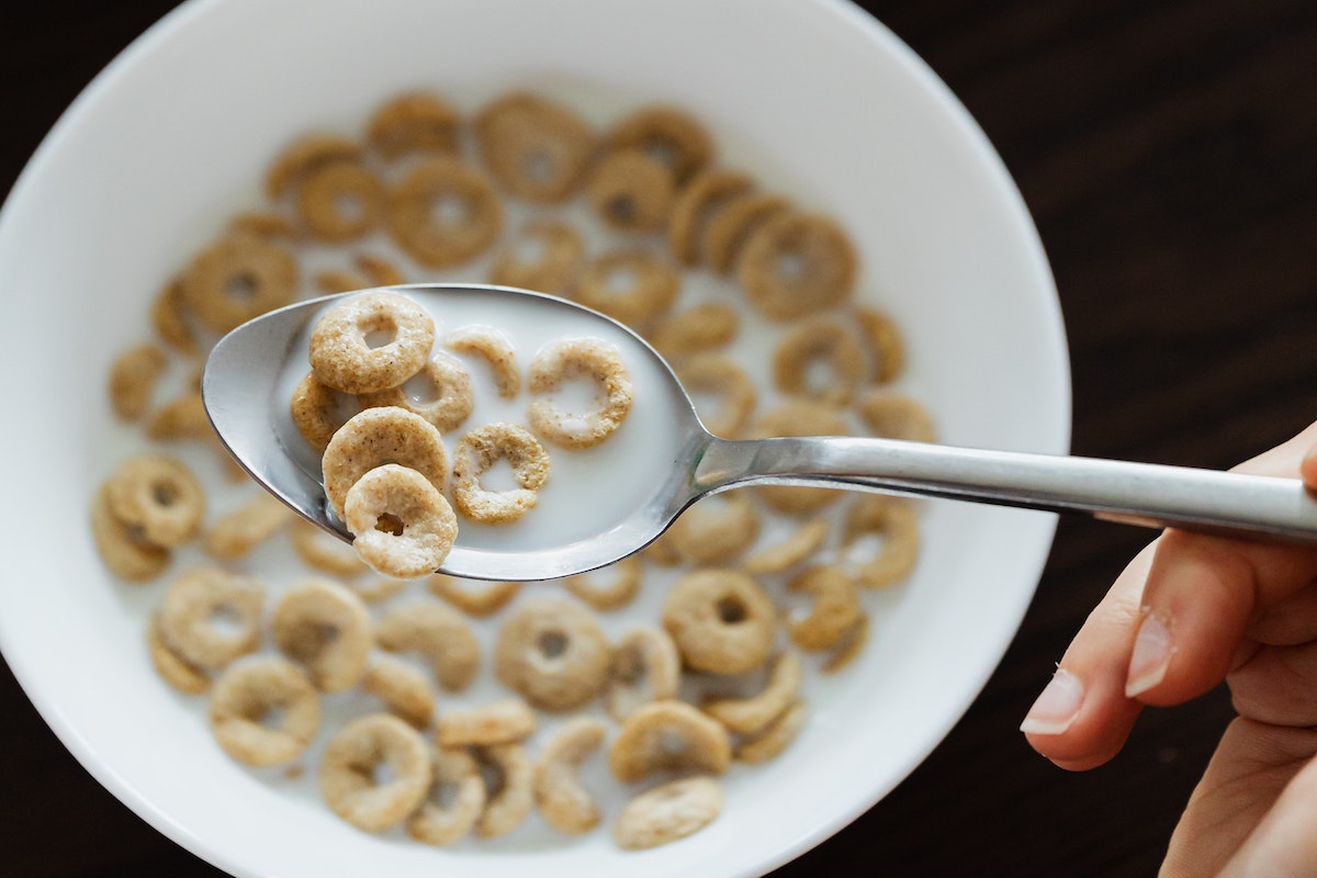 Person holding a spoon over a bowl of breakfast cereal in milk.