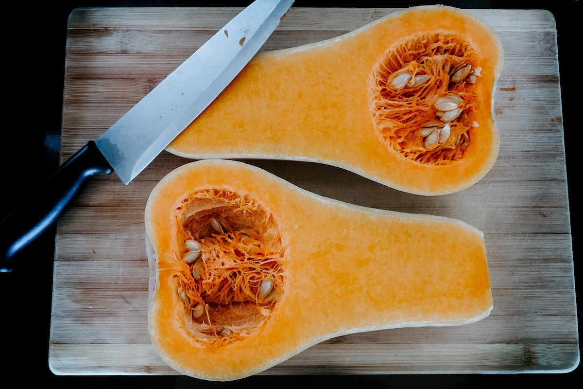 Butternut squash cut in half sitting on a cutting board.