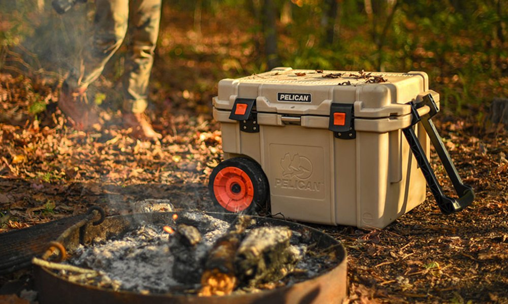 Pelican 45QW Elite Wheeled Cooler next to a campfire with a photographer blurred in the background.