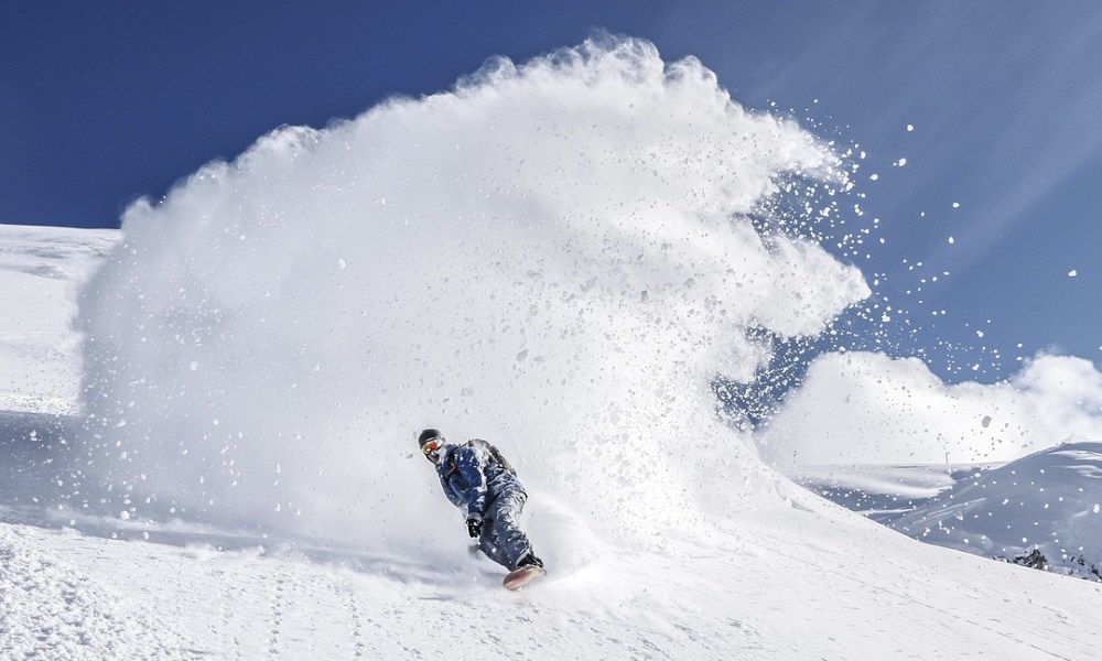 Person snowboarding down a mountain with a wake of snow behind them