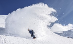 Person snowboarding down a mountain with a wake of snow behind them