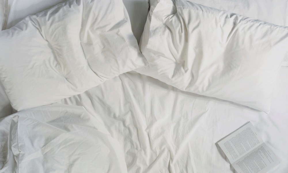 Two pillows and an opened book on a bed.