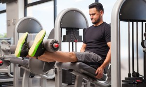 A male athlete doing leg extensions on a machine in a gym.