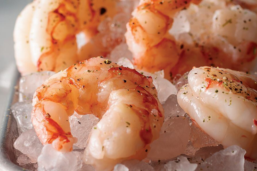 Close-up of four cooked shrimp sitting on ice.