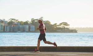 Man running on street by a body of water.