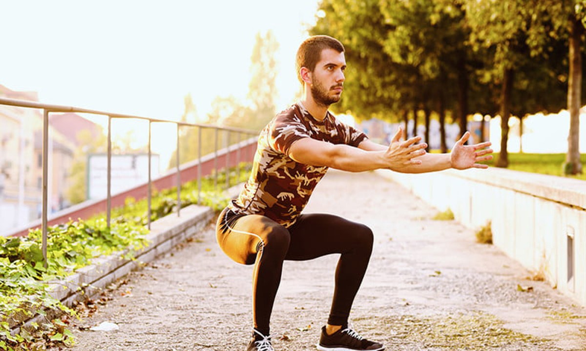 A man doing sumo squats in a park