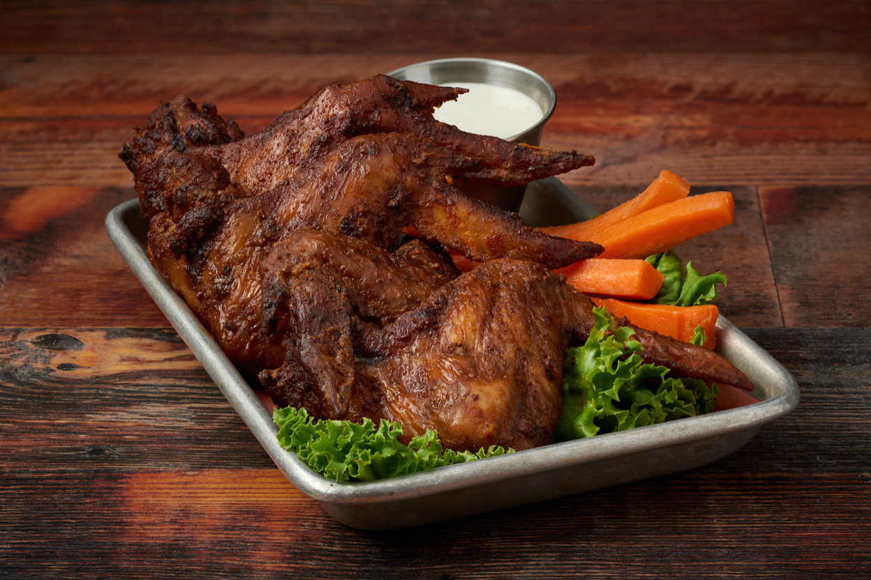 Virgil's smoked wings on a metal tray with raw carrots placed on a wooden table.