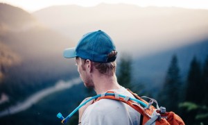 A runner with a hydration pack looks out over a rolling green wilderness.