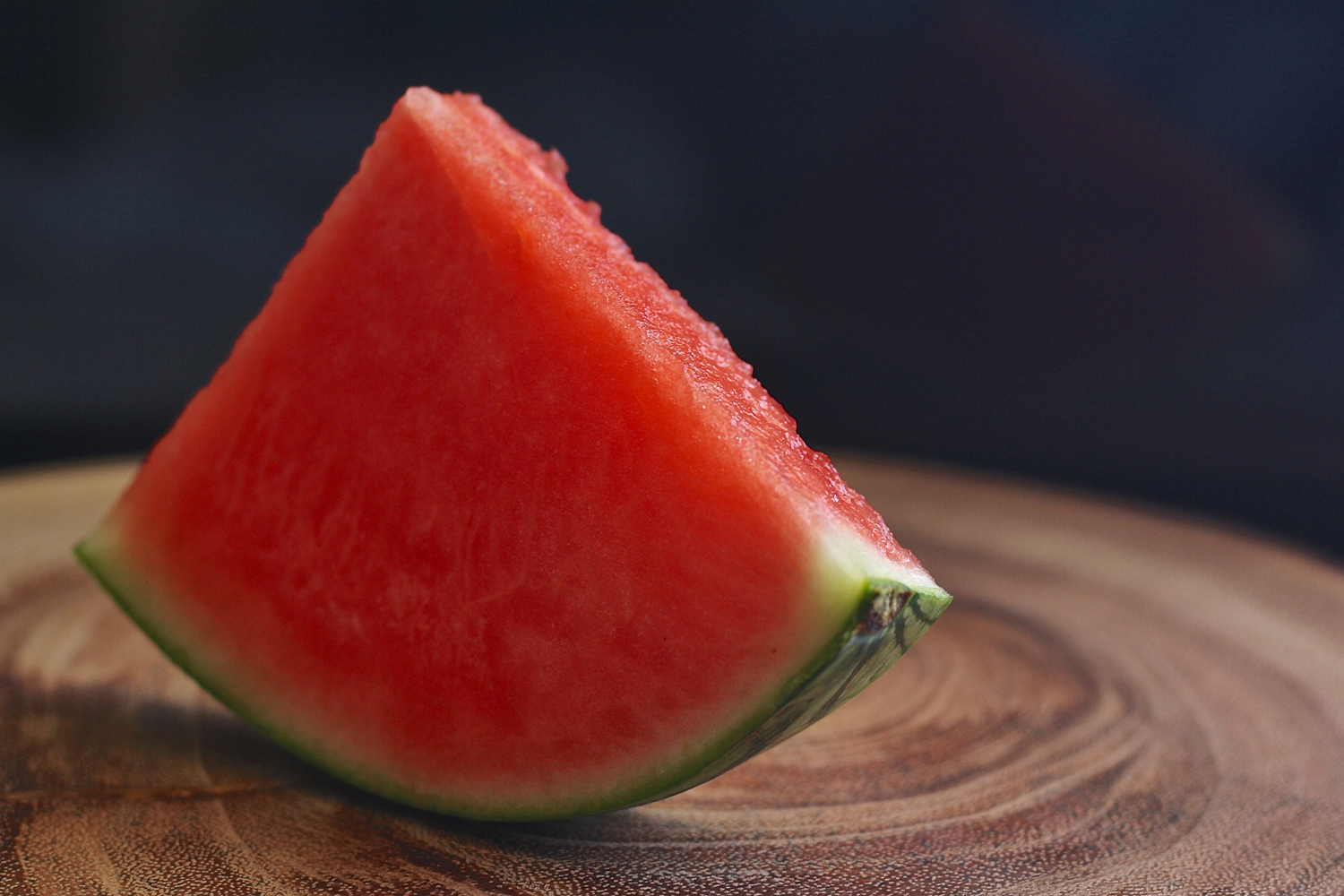 A close-up of a watermelon slice balanced on a wooden surface.