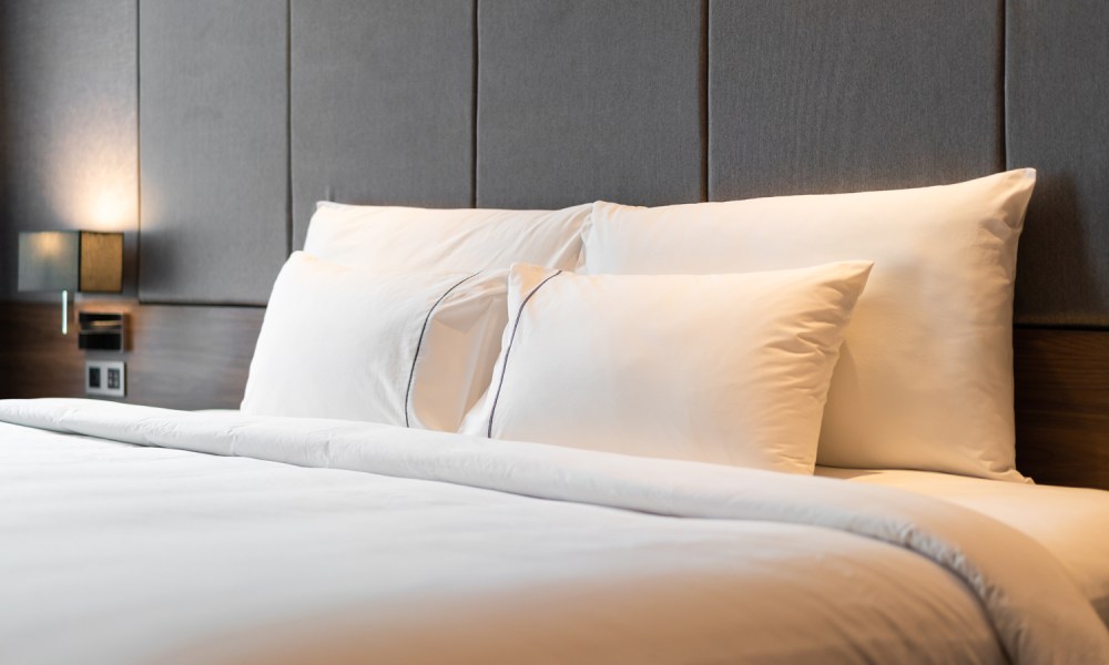 Four white pillows propped up on a bed in a room.