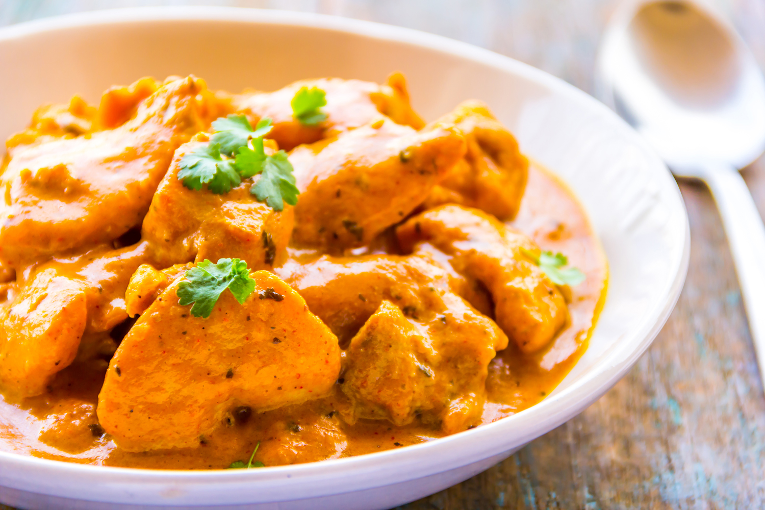 A close-up of a butter chicken served on a bowl with spoon on a table.