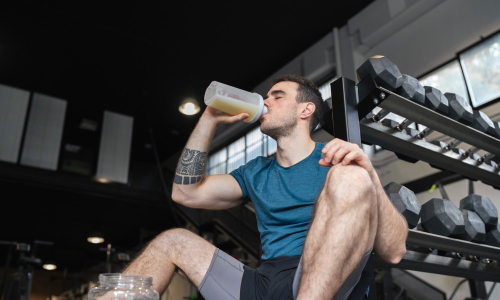 Male athlete drinking protein shake while sitting in gym.