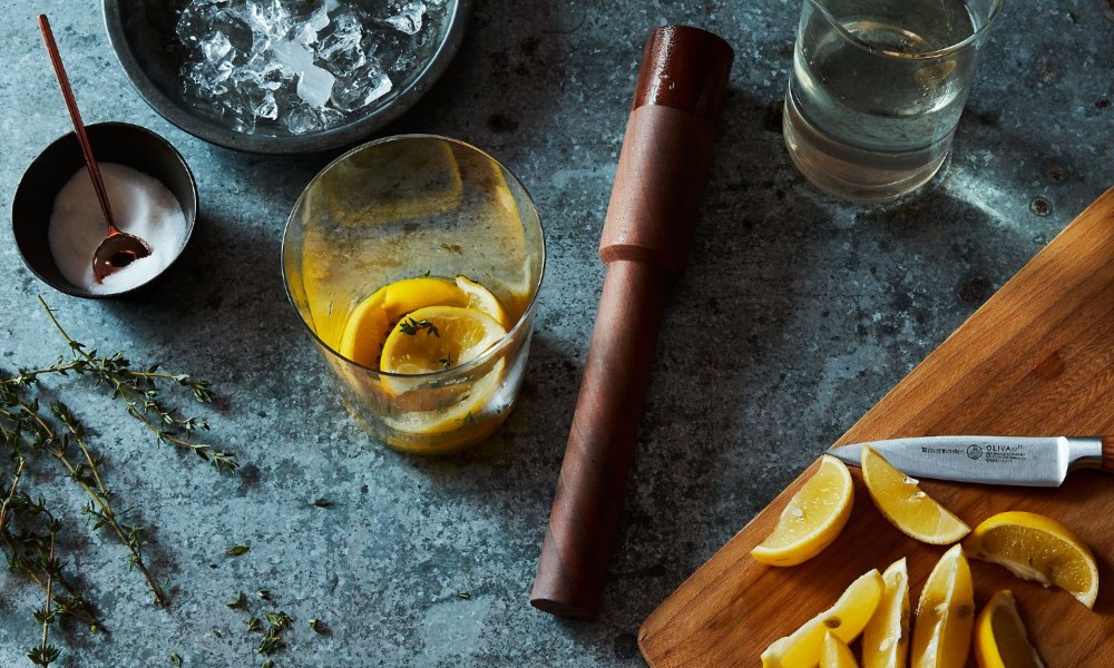 wooden muddler sitting on a table surrounded by garnishes and cocktails.