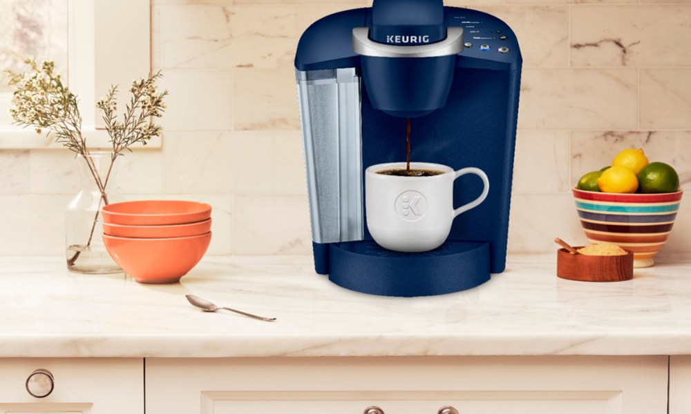 A blue Keurig K-Classic Single Serve K-Cup Pod Coffee Maker placed on a kitchen countertop with plants nearby.