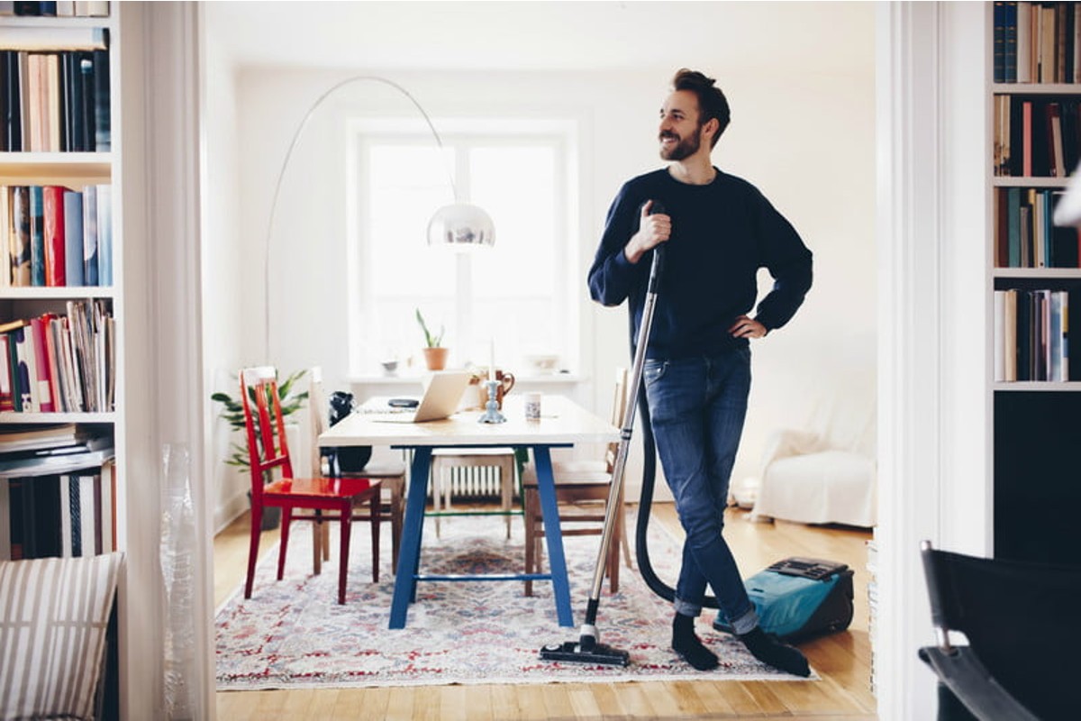 Man smiling in clean apartment holding a vacuum.