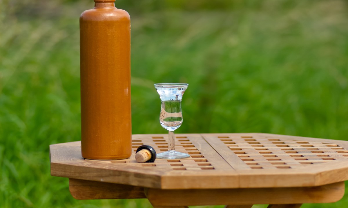 A bottle and a glass of genever on a wooden round table with grass as background