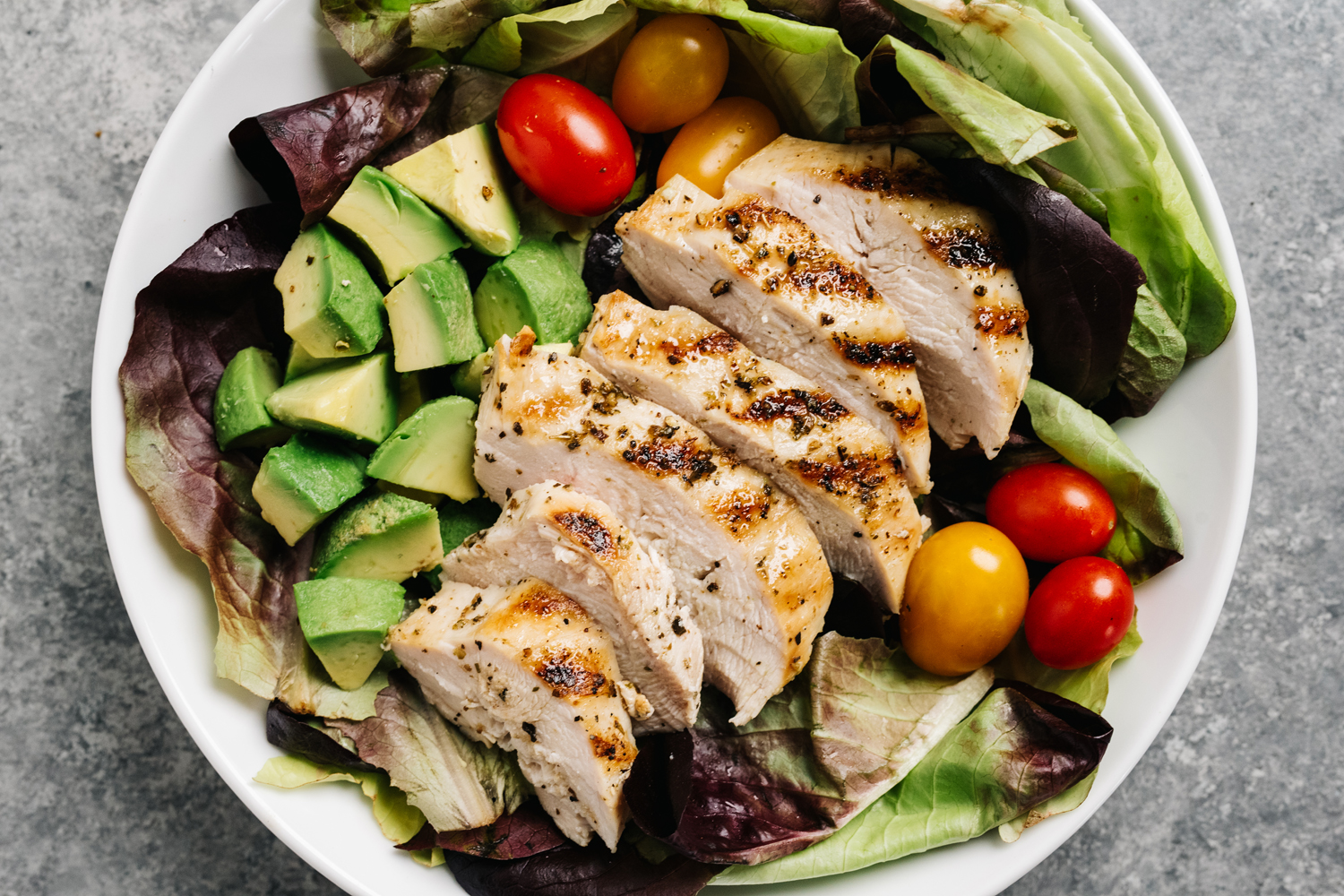 An overhead shot of a bowl of grilled chicken salad on a table.