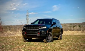 2022 Jeep Grand Cherokee Trailhawk front end from driver's side in front of bushes.