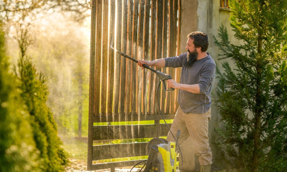 Man using a pressure washer to clean a gate.