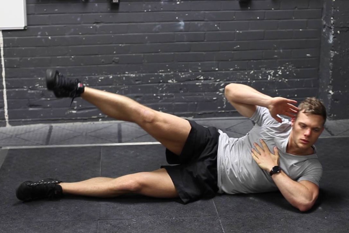 Man performing a side-jack knife on a rubber mat.