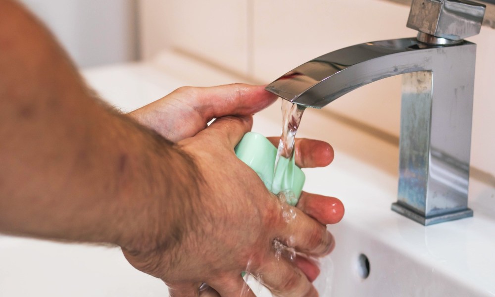 A man washes his hands with soap and water in a sink.