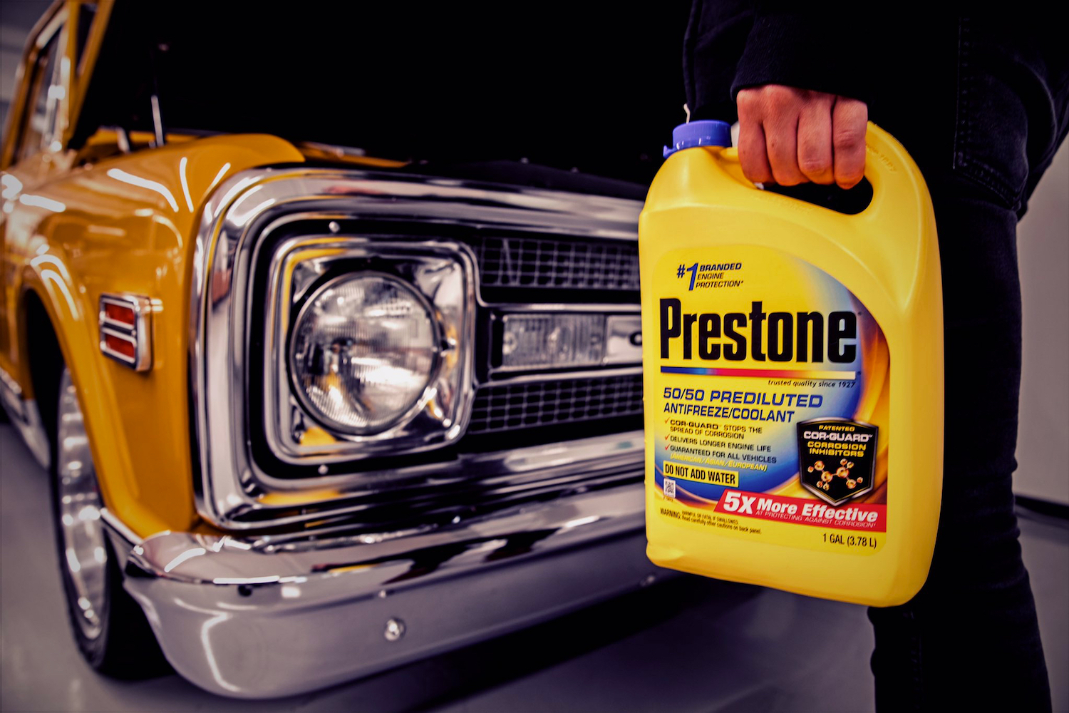 A jug of Prestone predicted 50/50 antifreeze/coolant in front of a yellow classic pickup truck in a garage.