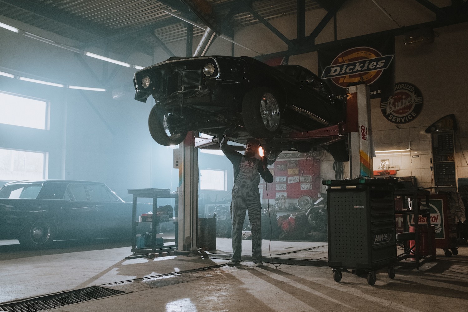 Mechanic working underneath a black classic muscle car in a garage. 