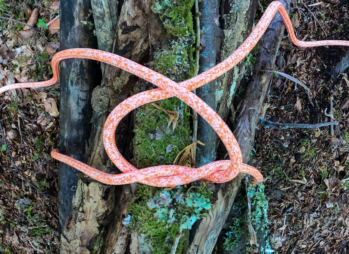 Step 4 of tying a square knot around a bundle of wood