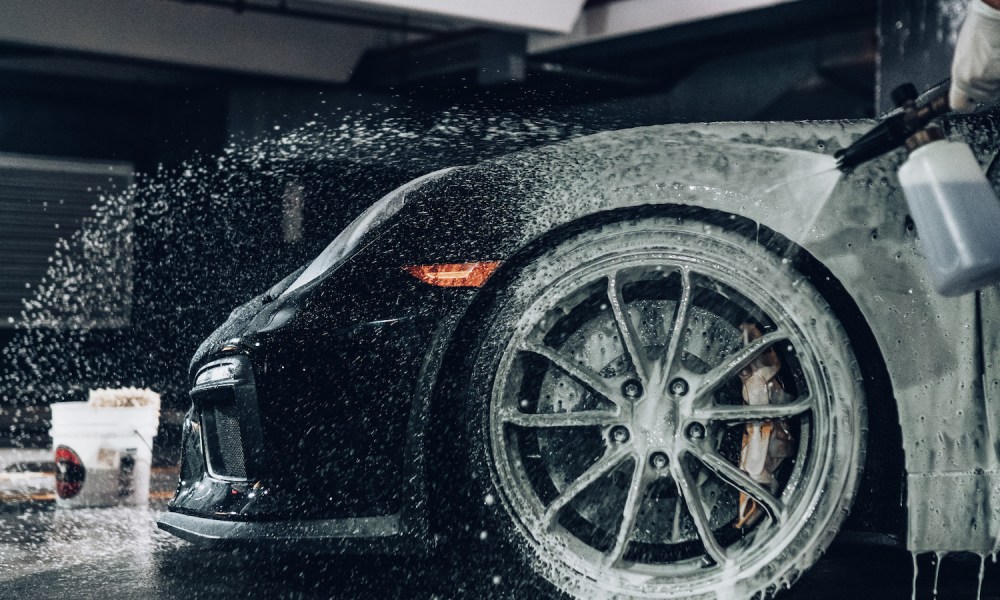 Close-up of front end tire of black Porsche 911 being washed with a spray foam gun