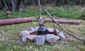 A campfire pot hanger holds a kettle over a stone circle