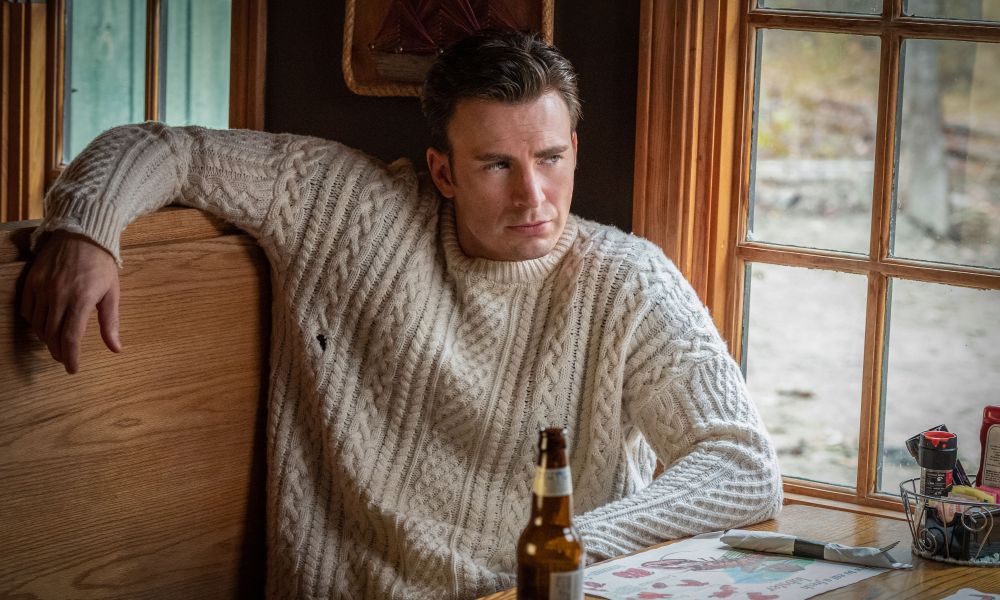 Chris Evans sitting at a table in a chunky knit sweater