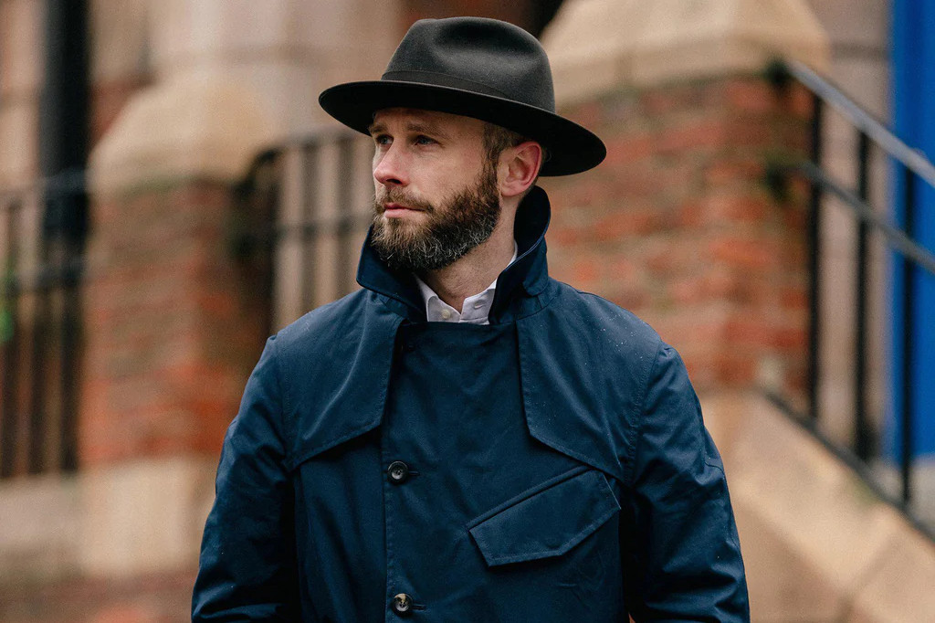 Man in a navy trench coat and brown hat.