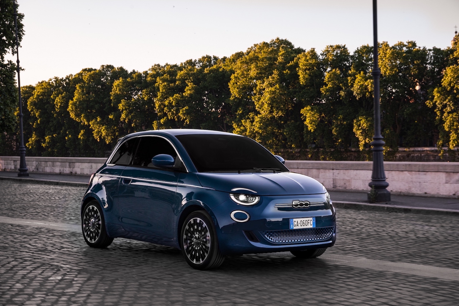 2024 Fiat 500e front end parked on a city street with bricks and trees in the back.