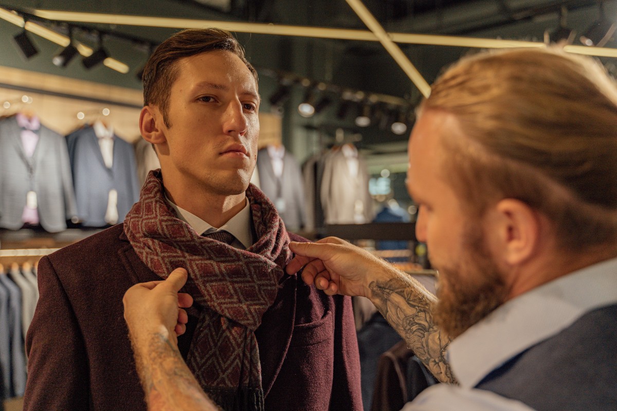 a man tying scarf for another man in store