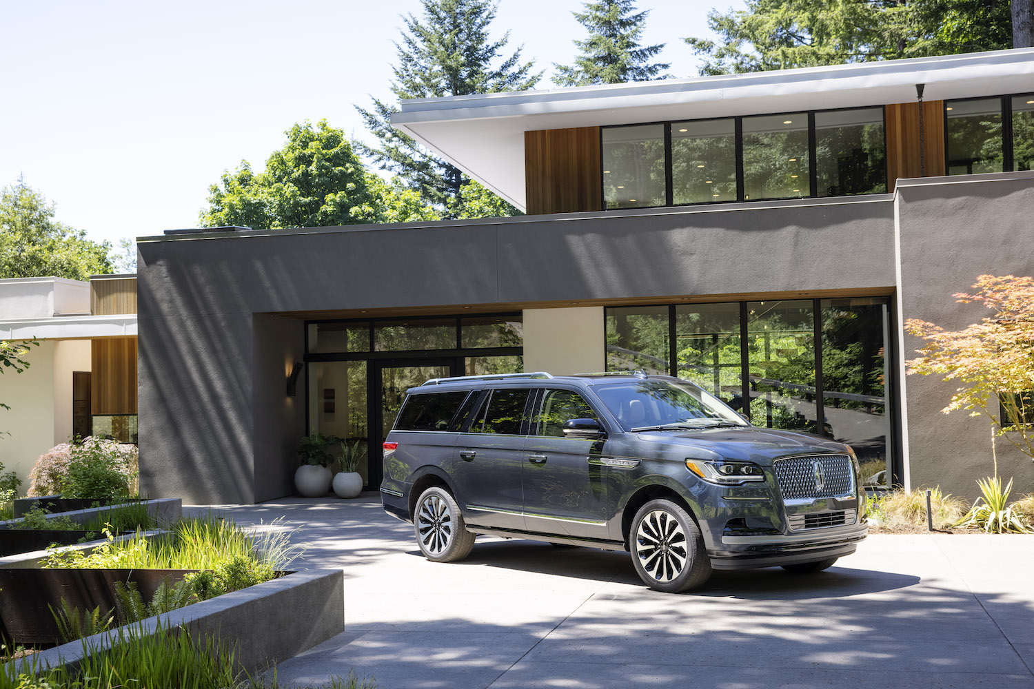 2022 Lincoln Navigator Flight Blue Reserve front end angle from passenger's side in front of a mansion with trees and blue skies in the back.