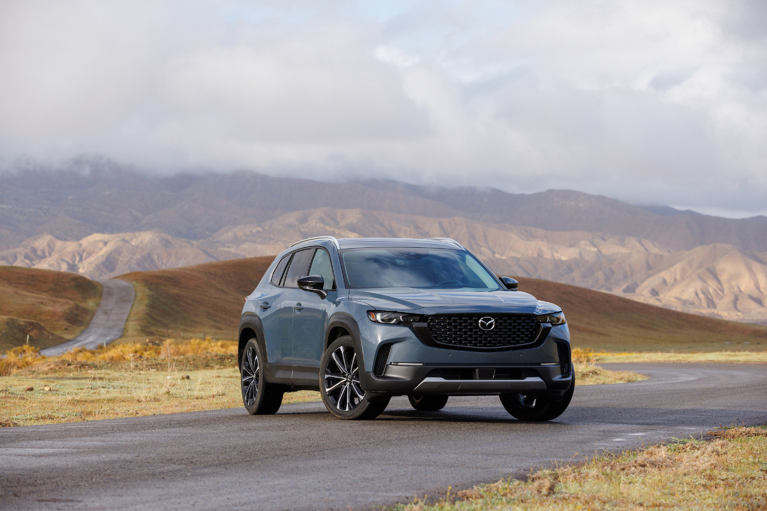 2022 Mazda CX-50 front end angle from passenger's side with rolling hills in the background with dark clouds.