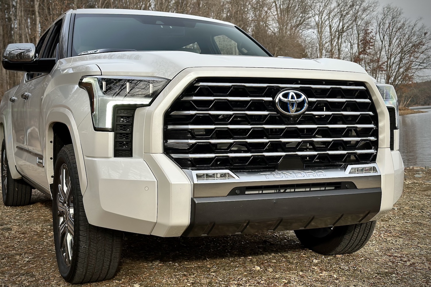 Close up of front grille on 2022 Toyota Tundra Hybrid Capstone parked on dirt with trees in the back.
