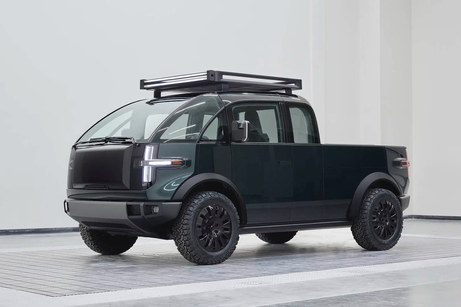 Canoo pickup truck front front end angle from driver's side in a studio with white walls in the back.