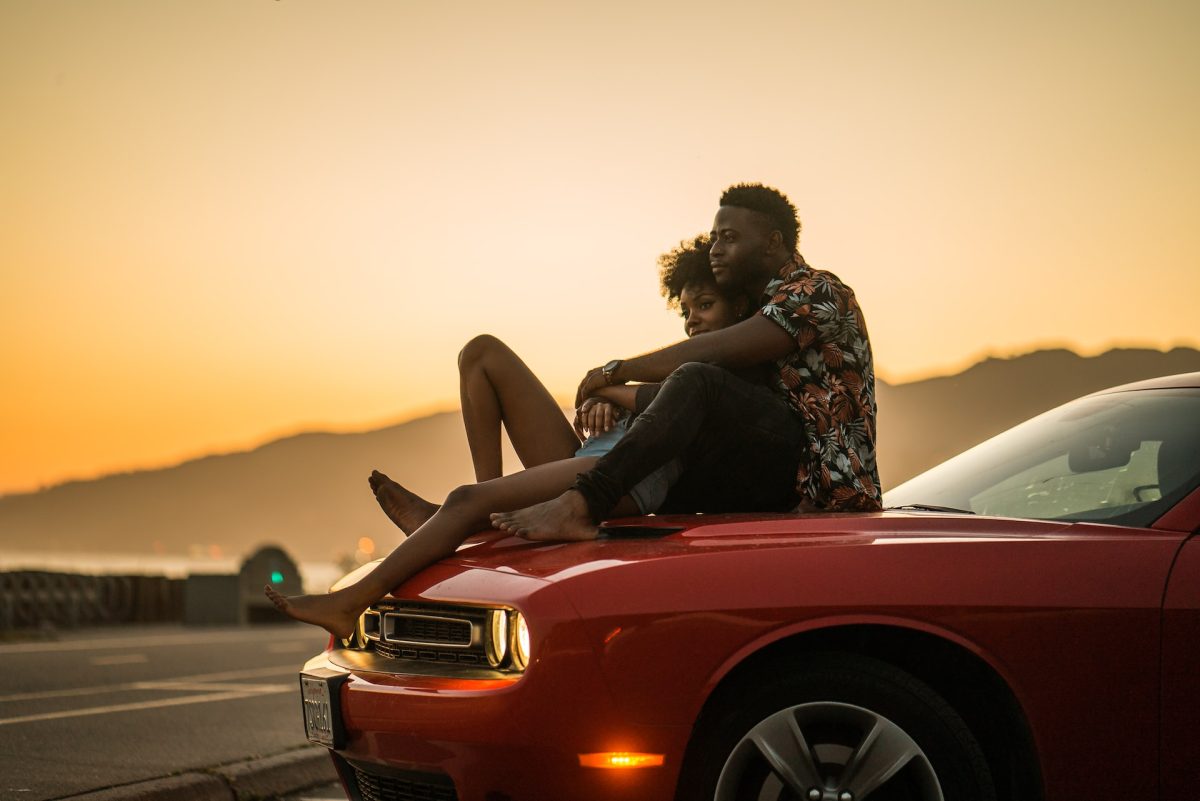 A couple relaxing in each other's arms while sitting on top of a car.