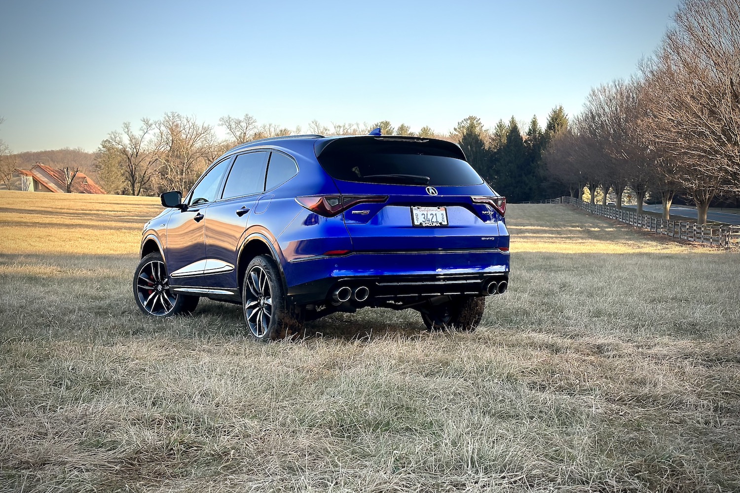 2022 Acura MDX Type S rear end angle from the driver's side parked in a field with trees in the back.